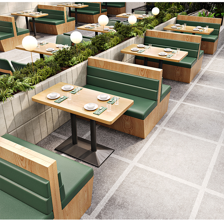 Modern restaurant booth seating with green upholstery and wooden accents, arranged alongside dining tables.