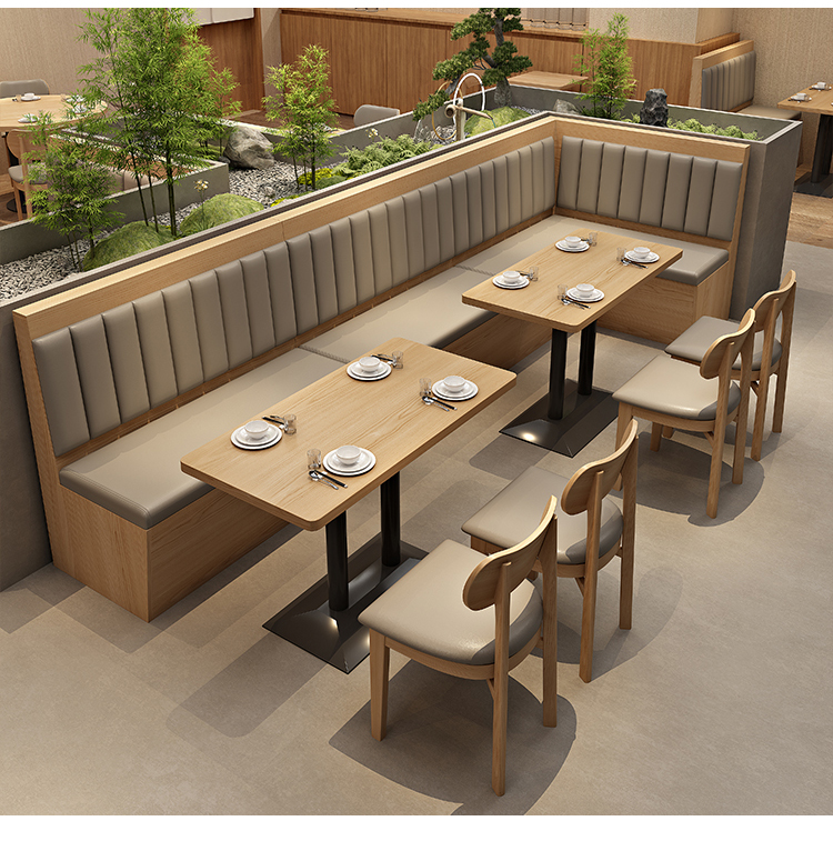 Restaurant booth seating with cushioned benches, wooden tables, and decorative greenery partition in a modern dining area.