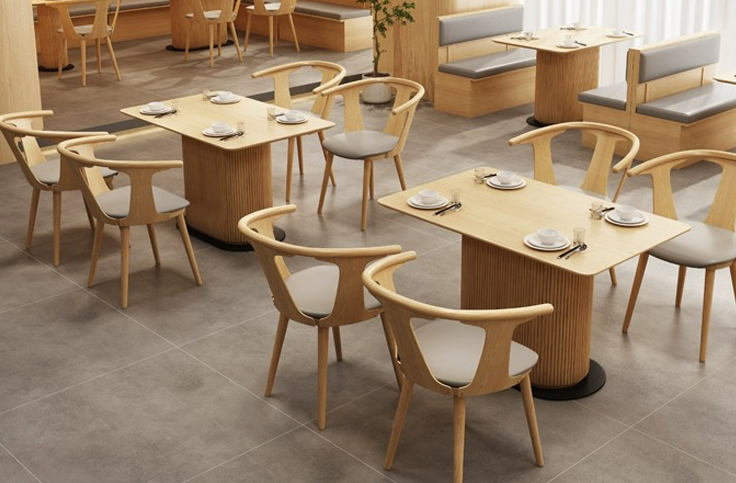 Modern coffee shop furniture with wooden round tables, curved armless chairs with light-colored cushions, and minimalist design style.