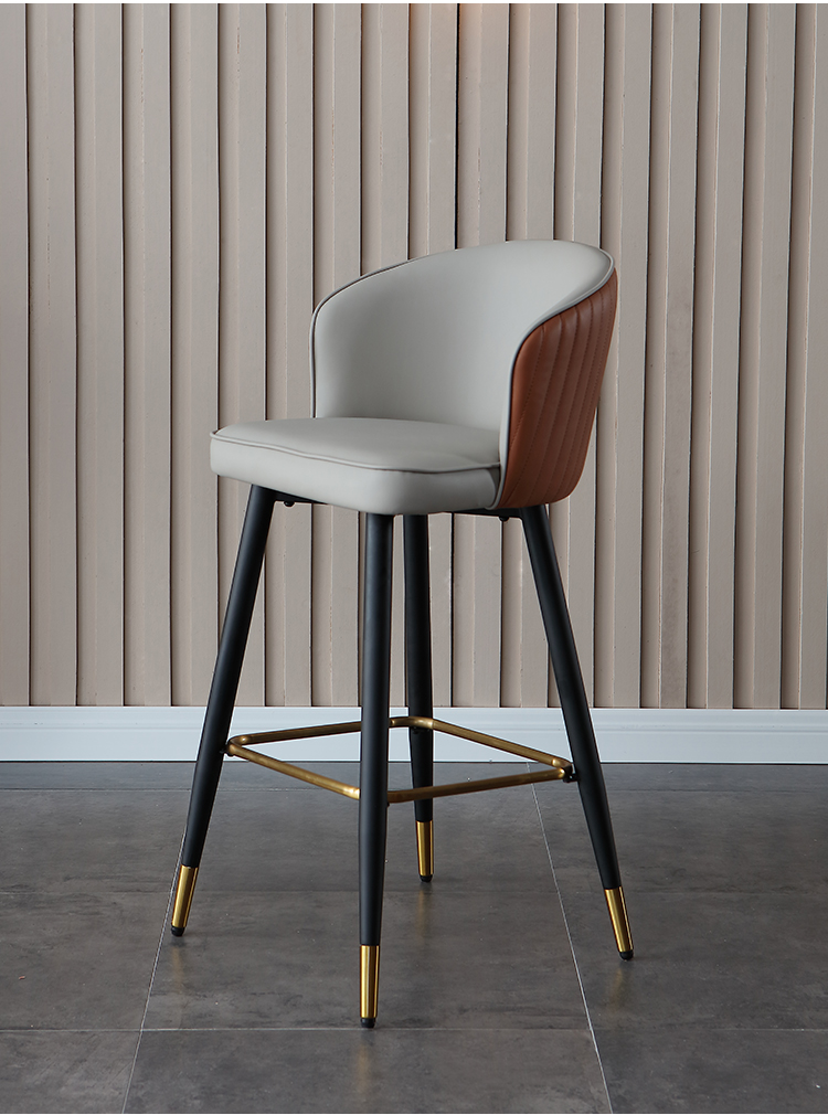 Modern bar stool with black metal legs, orange and gray PU leather seat and backrest with golden footrest, suitable for contemporary interiors.